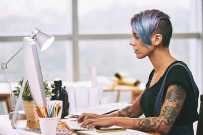 Side view of alternative style woman working on computer in office