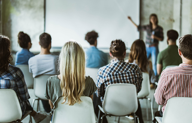 woman pointing to a whiteboard while standing in front of a room of students